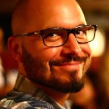 An individual with black glasses and a patterned shirt smiling 